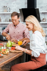 smiling couple preparing salad for dinner together and cutting vegetables in kitchen