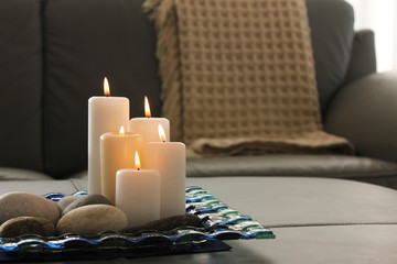 Burning candles, pebbles, glass  and gray sofa with blanket background. Interior decoration, living room.