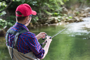Man fisherman catching trout in the river fishing rod. Fly fishing in a forest creek in Europe. Professional sport angler catches a fish.