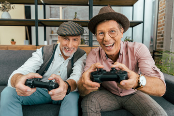 excited mature men playing with joysticks and smiling at camera