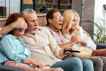 scared mature friends sitting on couch and watching tv together