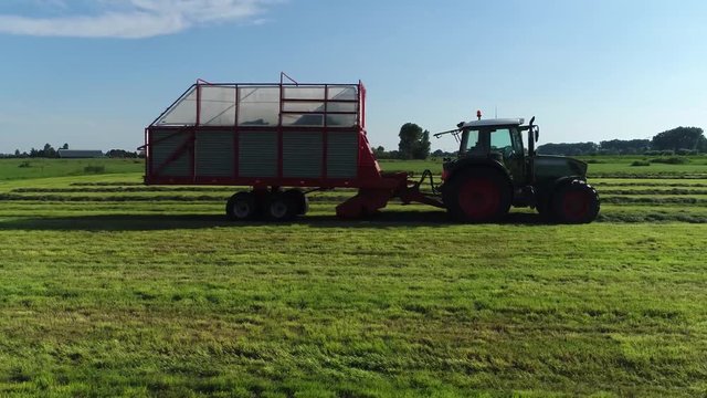 Low altitude aerial footage chaser bin also called grain cart or auger wagon is trailer towed by tractor with a built-in conveyor system used for pickup of dried crops from land in this case grass 4k