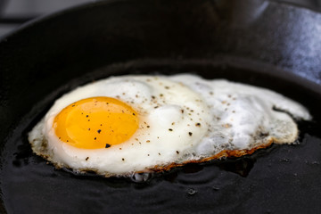 Closeup of fried egg in cast iron frying pan sprinkled with ground black pepper.