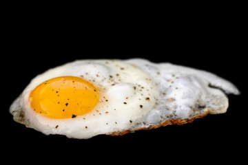 Single fried egg sprinkled with ground black pepper isolated on black.