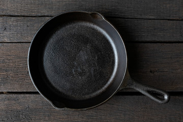 Empty black cast iron pan isolated on dark painted wood from above.