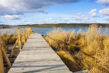 Wooden jetty with railings on the lake named Gurino in Siberia with a cloudy blue sky and golden reed