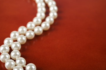 White pearl necklace on red leather background.