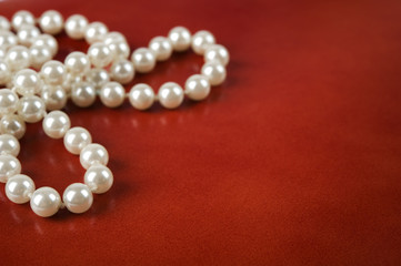 White pearl necklace on red leather background.