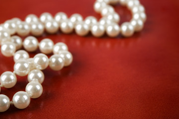 White pearl necklace on red leather background.