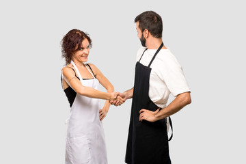 Couple of cooks shaking hands for closing a good deal on grey background