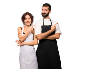Couple of cooks pointing to the side with a finger to present a  on isolated white background