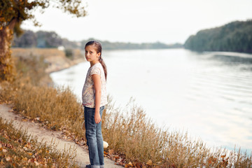 the girl child with toy bear walking along the path in the forest at sunset, beautiful river and landscape