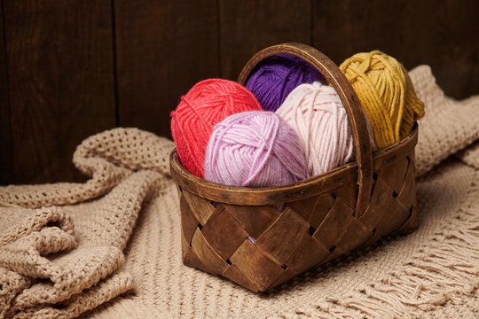 colorful wool yarn for knitting in basket, wooden background