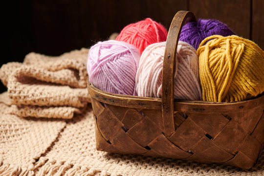 colorful wool yarn for knitting in basket, wooden background
