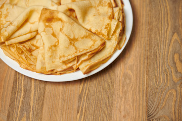Crepe closeup, heap of thin pancakes on a dish, wood background