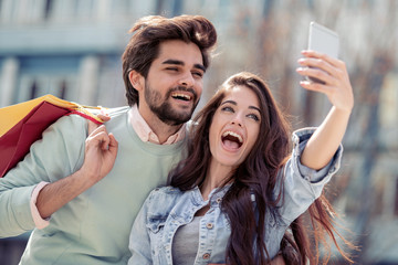 Happy couple taking selfie after shopping in the city