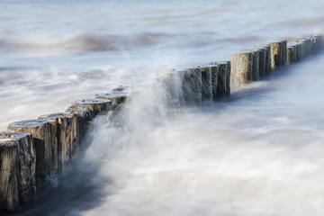 wooden groynes in the spray of the sea, smooth water by long exposure, nature background with copy space