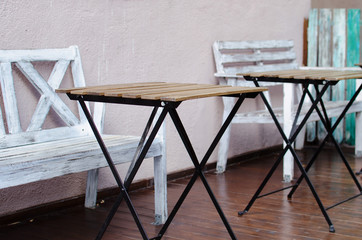 small wooden tables on metal legs and white benches of a street cafe. cozy coffee shop. colorful planks background