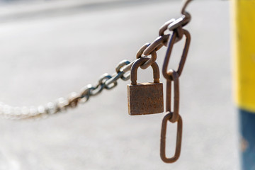 Fototapeta na wymiar Close-up of a rusty chain with a closed lock on a blurred background. old metal chain. denuction