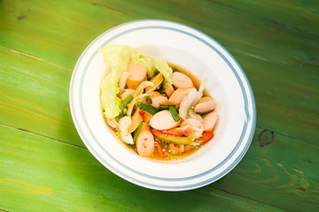 Sausage spicy salad in a bowl put on the green table.