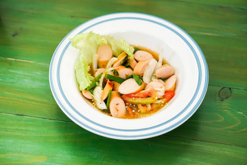 Sausage spicy salad in a bowl put on the green table.