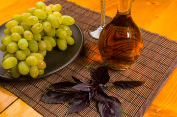 large brush of green grapes in a ceramic plate, a decanter and a glass of wine and cheese