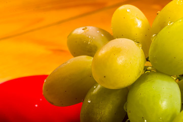large brush of green grapes in a red ceramic plate on a wooden background