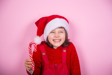Cute smiling little girl in Santa hat and Christmas costume holding caramel can in studio on pink background.