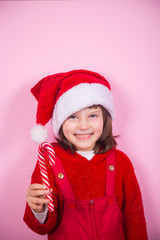 Cute smiling little girl in Santa hat and Christmas costume holding caramel can in studio on pink background.