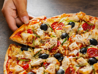 woman Hand takes a slice of Pizza with Chicken meat, Mozzarella cheese, tomato, olive. Italian pizza on wooden background