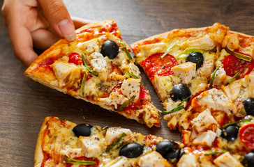 woman Hand takes a slice of Pizza with Chicken meat, Mozzarella cheese, tomato, olive. Italian pizza on wooden background