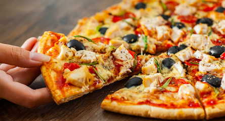 woman Hand takes a slice of Pizza with Chicken meat, Mozzarella cheese, tomato, olive. Italian pizza on wooden background