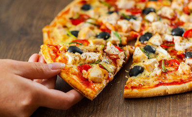 woman Hand takes a slice of Pizza with Chicken meat, Mozzarella cheese, tomato, olive. Italian pizza on wooden background