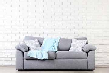 Modern grey sofa with pillows and plaid on brick wall background