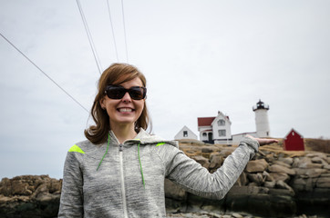 Woman smiles and holds the Nubble Lighthouse in a forced perspective view in York Maine
