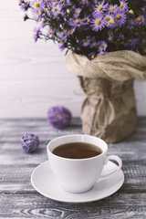 Romantic background with a cup of tea, lilac flowers in a vase on a gray wooden table