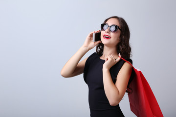 Happy woman with red shopping bag and smartphone on grey background