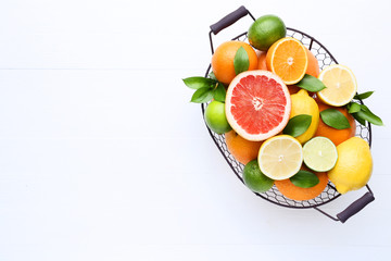 Citrus fruits with green leafs in basket on white wooden table