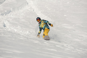 Young snowboarder in bright sportswear riding down a snow hill on bright winter day