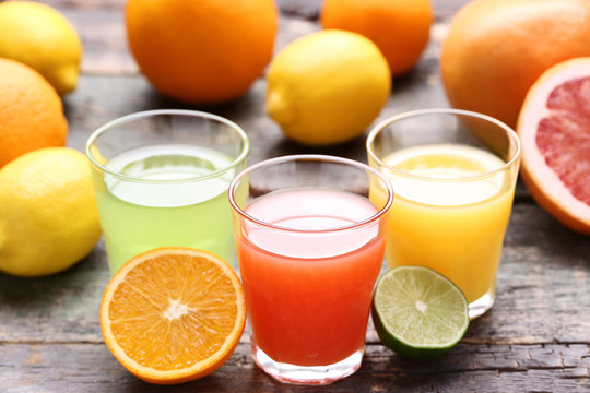 Citrus juice in glasses with fruits on grey wooden table