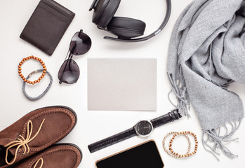 Flat lay of men's accessories with shoes, watch, phone, earphones, sunglasses, scarf over the orange background