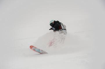 Professional snowboarder riding down the pure mountain slope in powder