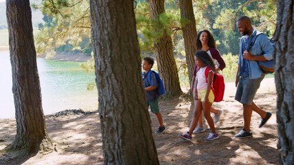 Family On Hike Walking Along Path Through Woods Next To Lake