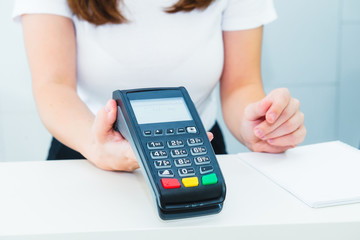 Seller holds payment terminal in hands. Contactless payment with nfc technology at shop, clinic, hotel. Mobile payment PayPass. Selective Focus on hands. Copy space. - obrazy, fototapety, plakaty