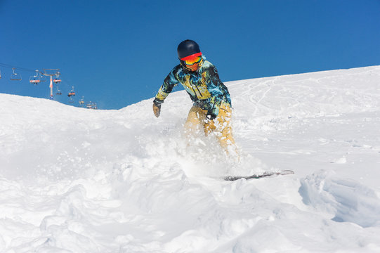 Professional active snowboarder in bright sportswear riding down a mountain slope