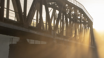 A railway bridge in the morning fog or smoke through which the rays of the sun shine