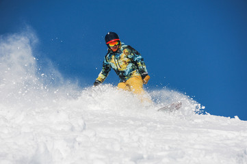 Snowboarder in bright sportswear riding down a powder mountain slope