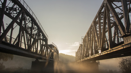 Fototapeta premium A railway bridge in the morning fog or smoke through which the rays of the sun shine