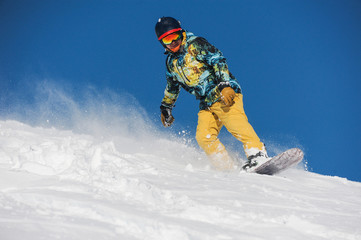 Active snowboarder in bright sportswear riding down a powder mountain slope