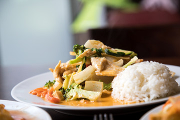 Rotes Thai Curry aus Wok mit Huhn, Gemüse und Reis im Restaurant